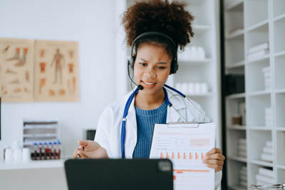 Attractive African female doctor talking while explaining medica Doctor talking while explaining medical treatment to patient through a video call with laptop in office